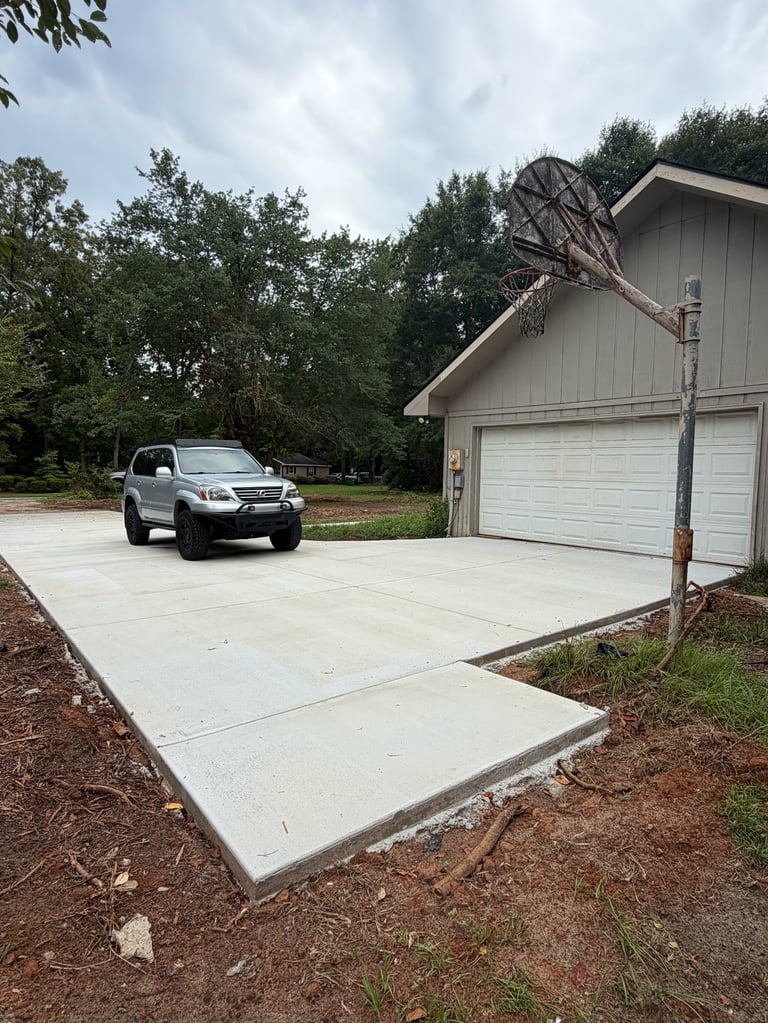 White SUV parked on concrete driveway in front of gray two-car garage surrounded by trees