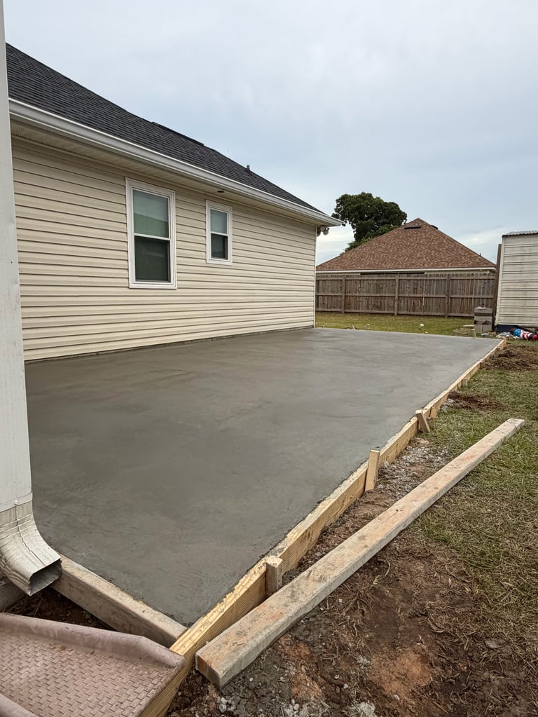 New concrete patio next to residential house with wooden forms and landscaping