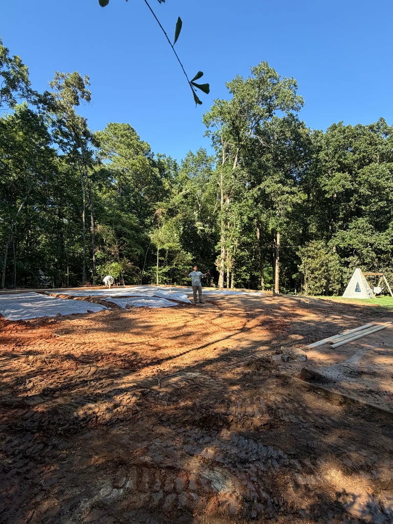 Camping ground with brown dirt area, tent, blue canopy, and tall trees under clear sky